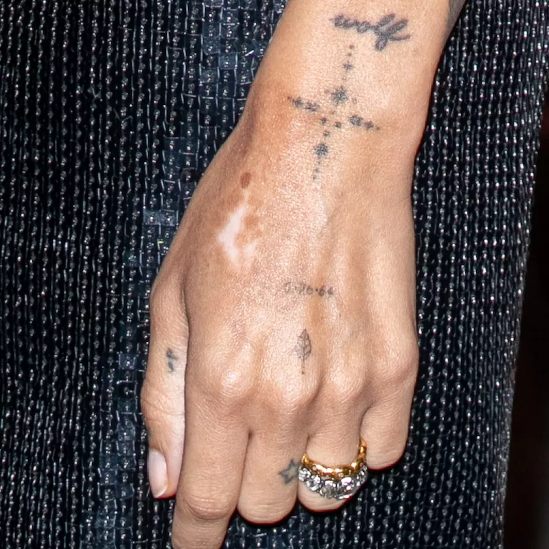 Tattoos on Zoe Kravitz's hand, including wolf word tattoo, compass, and date