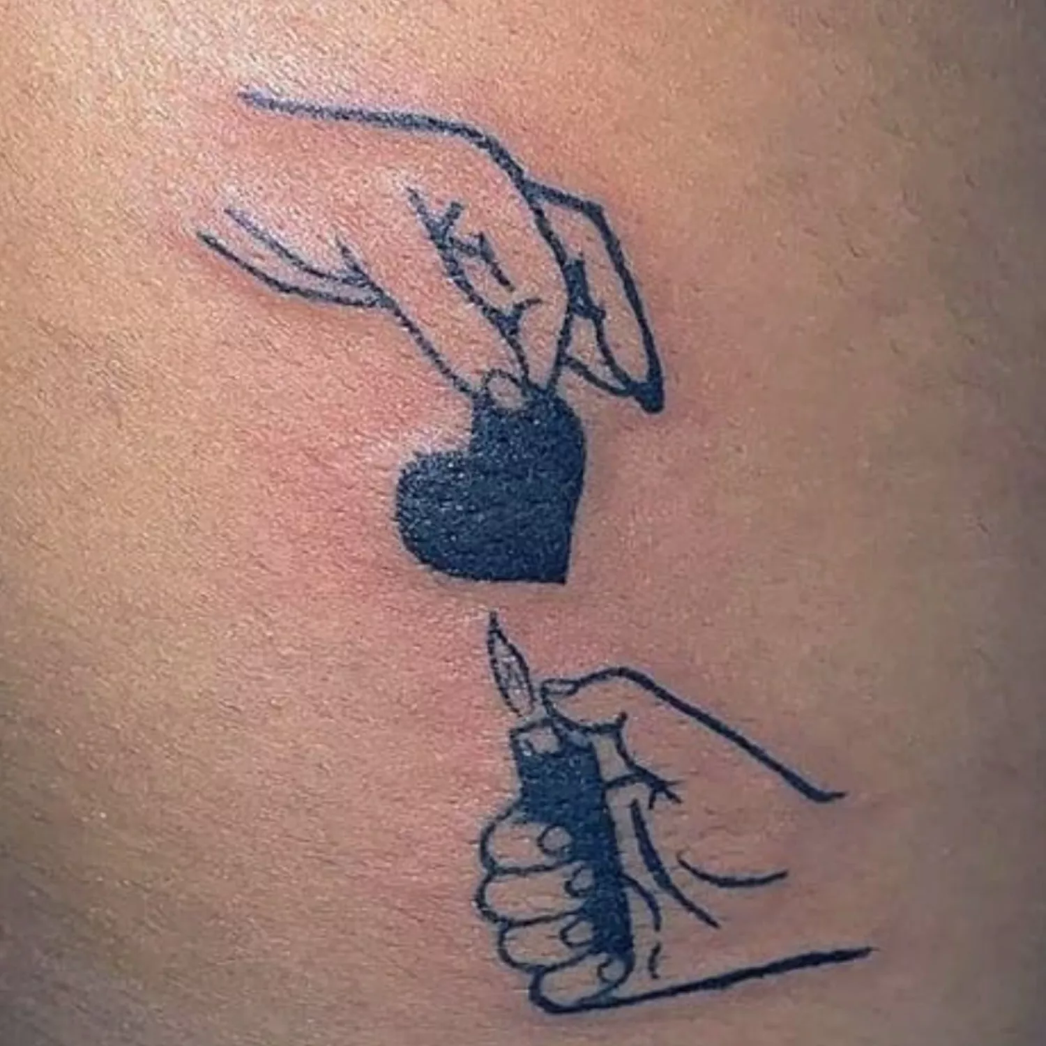 A tattoo of a hand holding a heart and another hand lighting up a lighter below it.