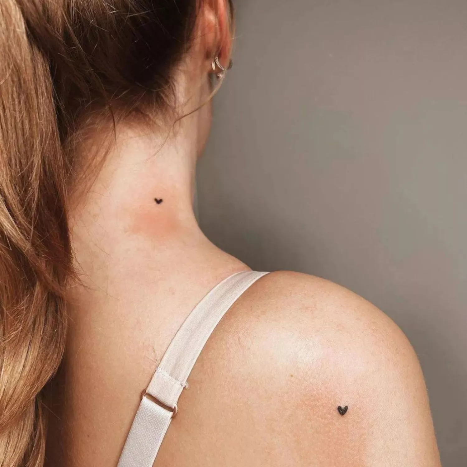 Two tiny heart tattoos on the neck and the shoulder, almost freckle-like.