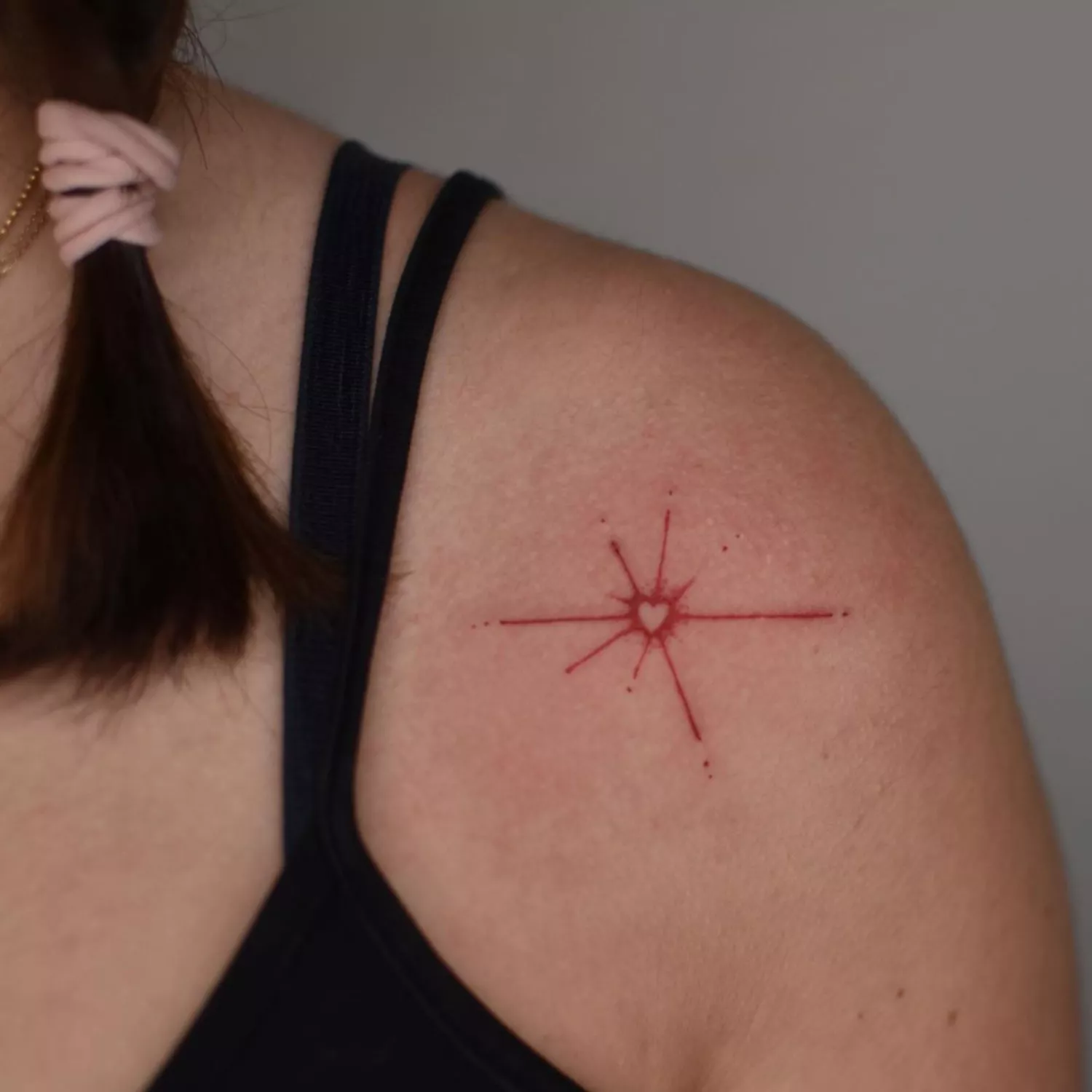 A red tattoo on a shoulder of a shooting star with a heart in the middle.