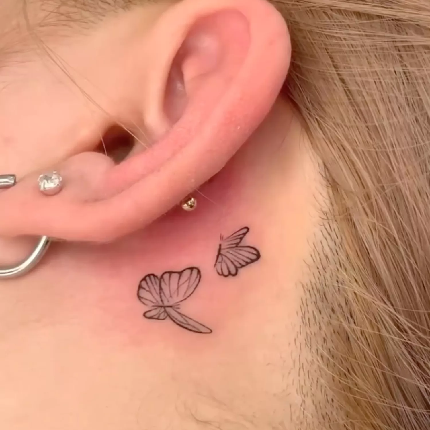 zoomed-in photo of person with two butterflies tattoo behind the ear