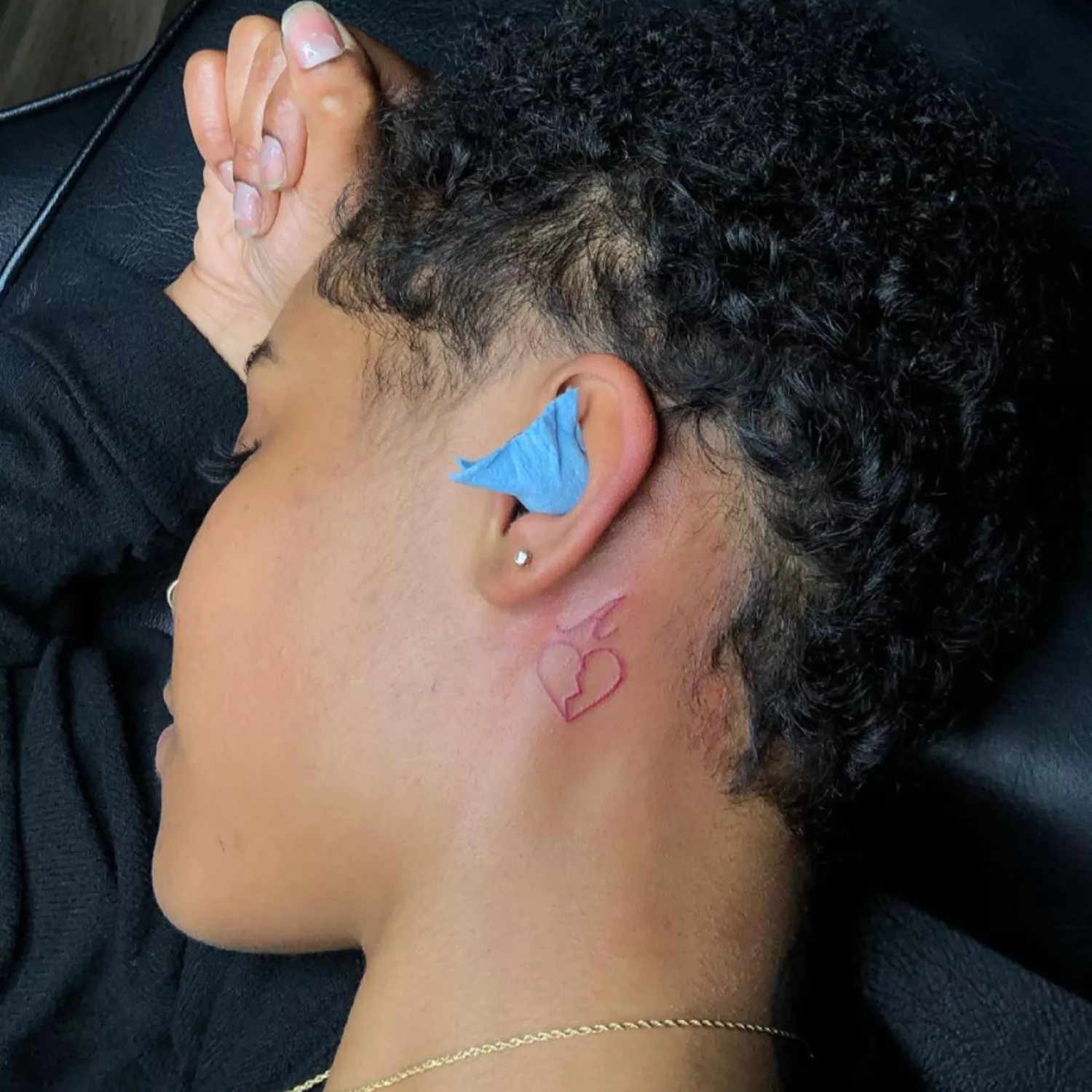 zoomed-in photo of person with red ink broken heart tattoo behind the ear