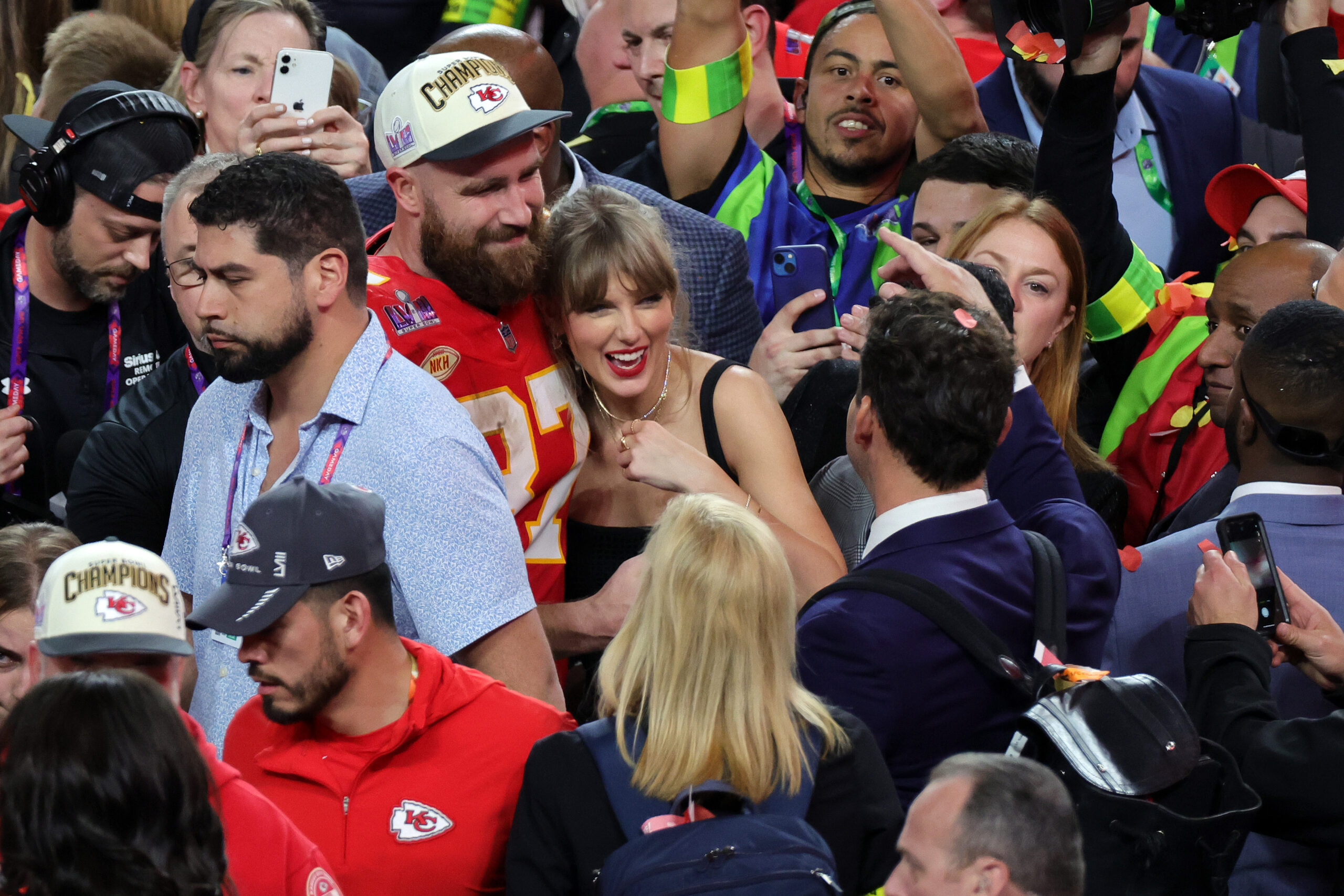 Travis Kelce with his arms around Taylor Swift in a swarm of people