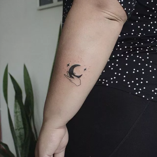 hand holding the bottom of a crescent moon tattoo