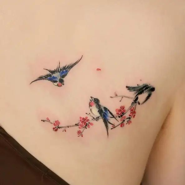 This may contain: two birds on a branch with red flowers and leaves around the neck tattoo designs for women