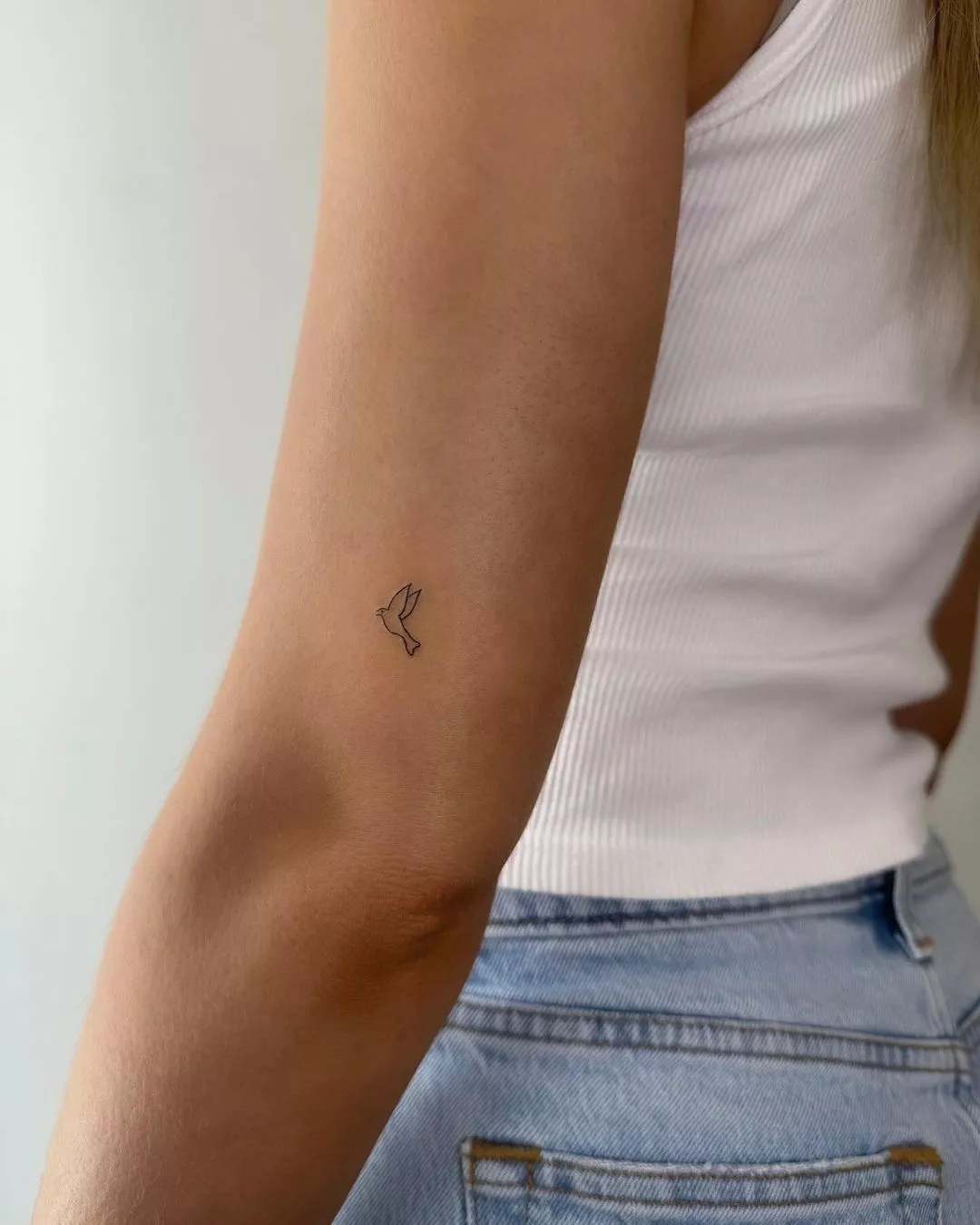 Person showing off the tiny tattoo of a flying dove on the back of their arm