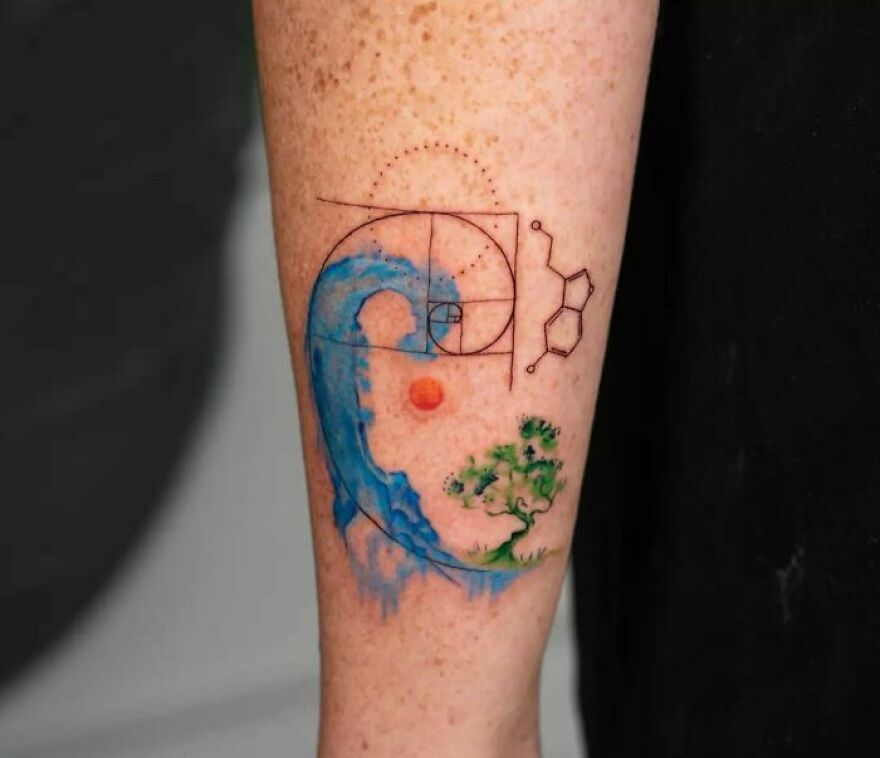Watercolor tattoo on forearm featuring a blue wave, geometric lines, a tree, and a small orange sun.