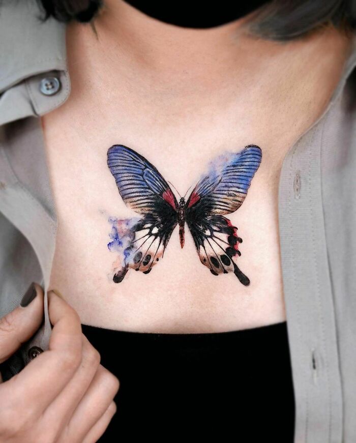 Colorful butterfly tattoo on a person's chest, featuring vibrant blue and red hues.
