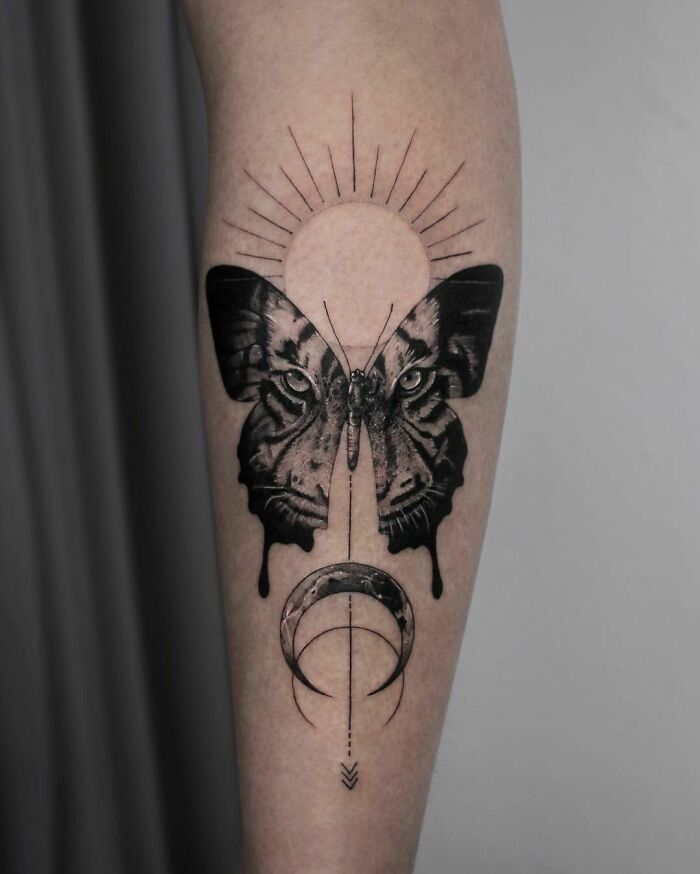 Minimalist butterfly tattoo with celestial elements on forearm, showcasing intricate black ink design.
