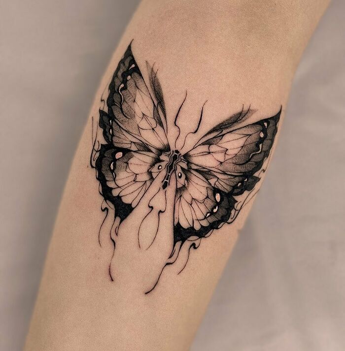 Black and white butterfly tattoo on forearm, showcasing intricate and artistic design.