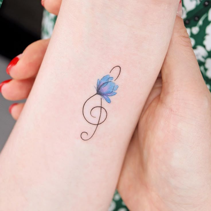 This may contain: a woman's arm with a blue flower tattoo on the left side of her wrist