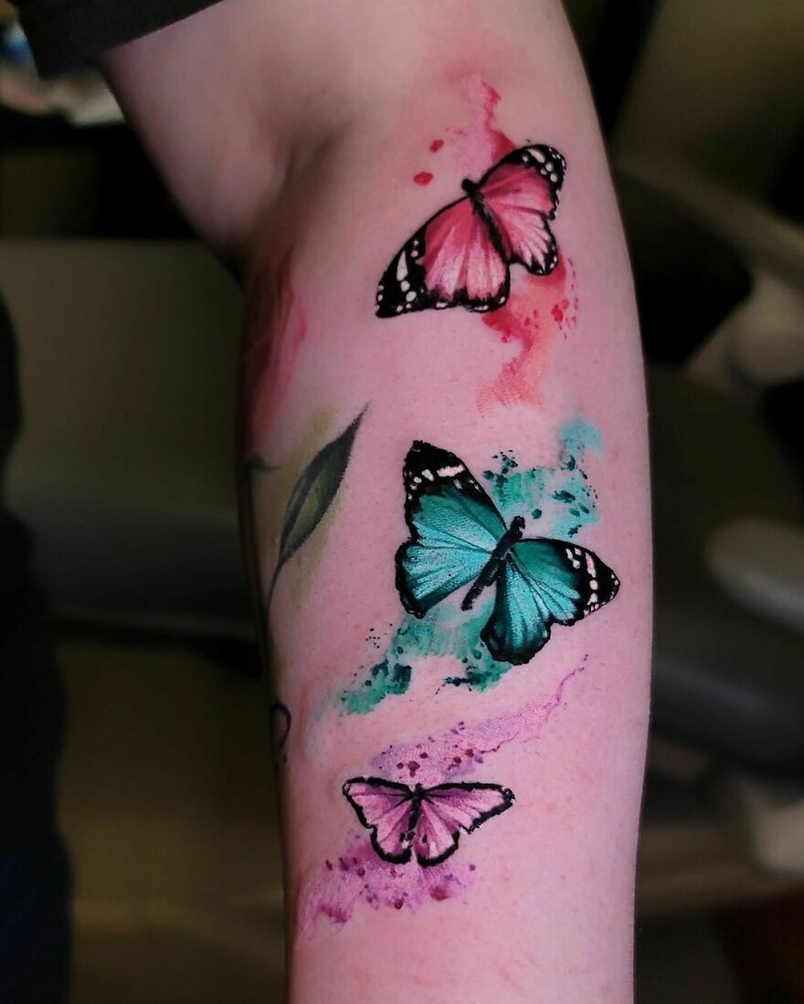 Arm with vibrant watercolor tattoo featuring pink and blue butterflies.