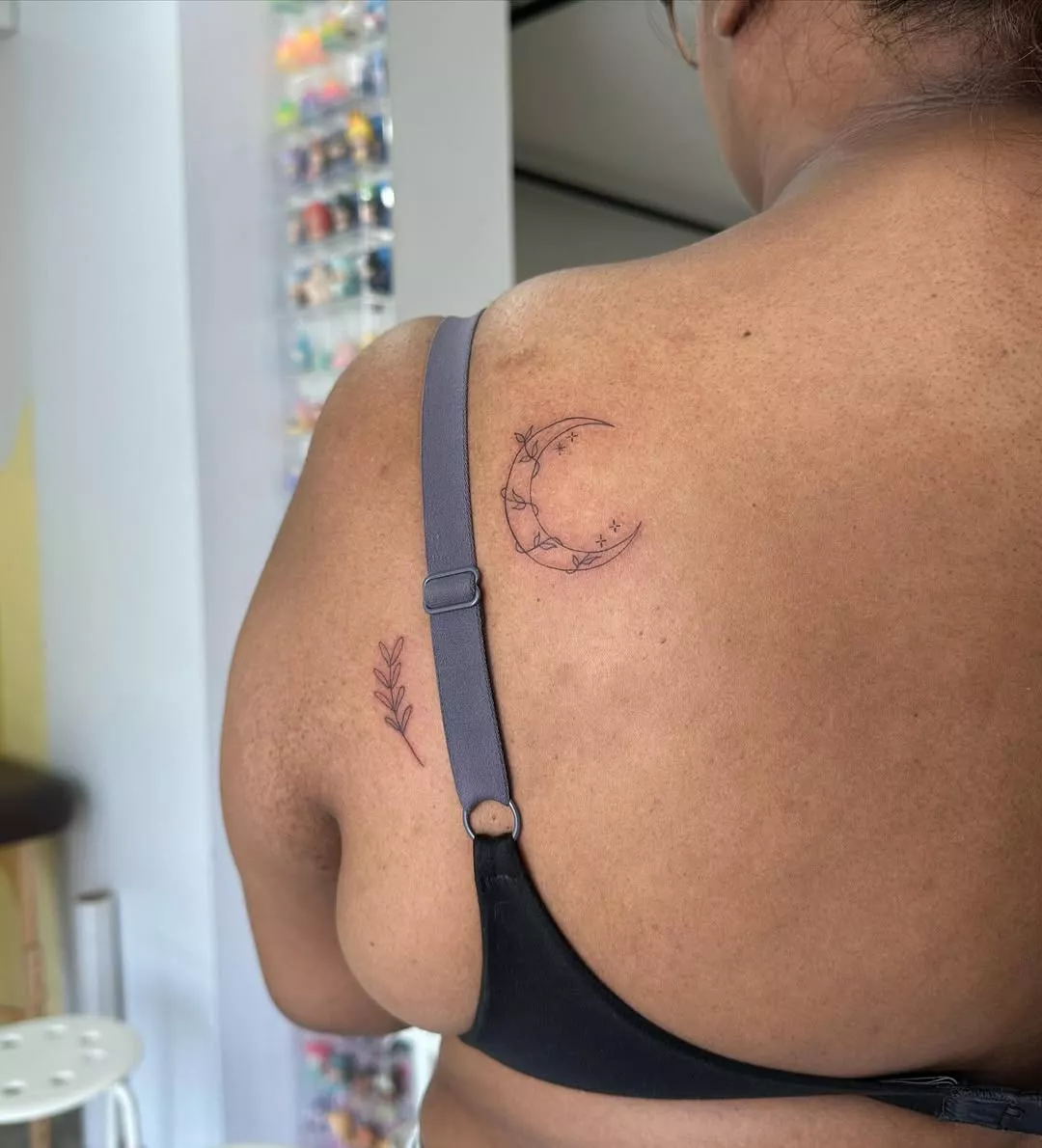 Person facing away from the camera to show the tiny tattoos of a moon and a plant on their back