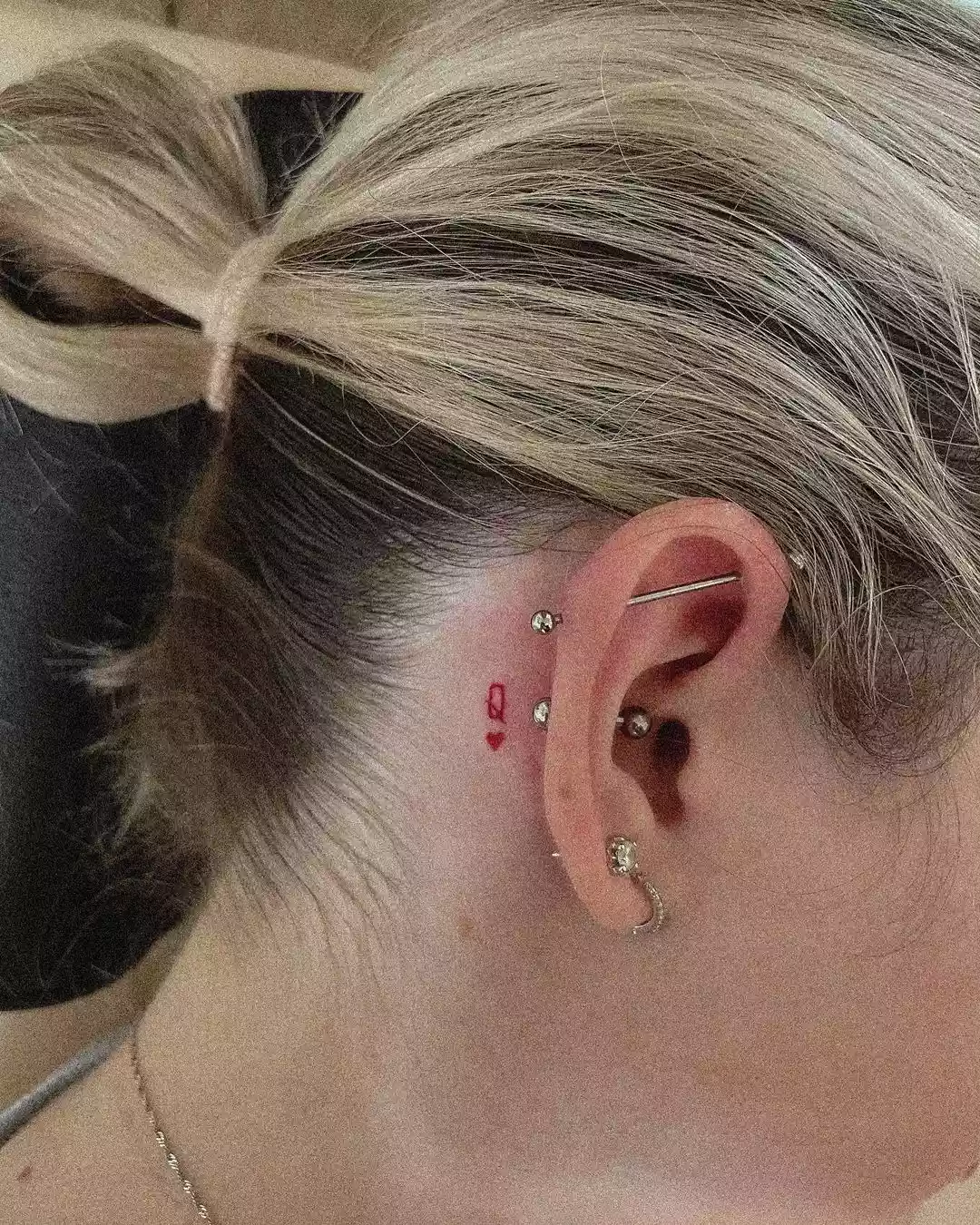 Person showing off the tiny tattoo on the back of their ear, which is a red Q on top of a heart