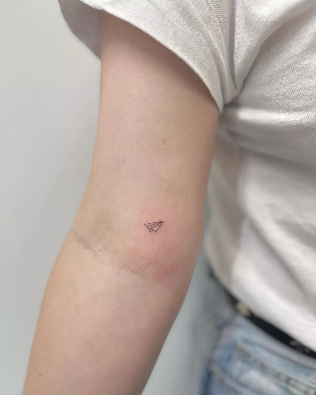 Person shows off the tattoo on the inside of their elbow, which is a small paper plane