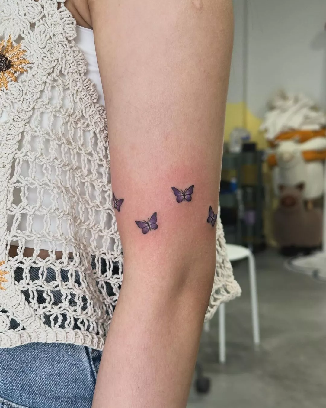 Person showing off their tiny butterfly tattoos, which are arranged as a band around the arm