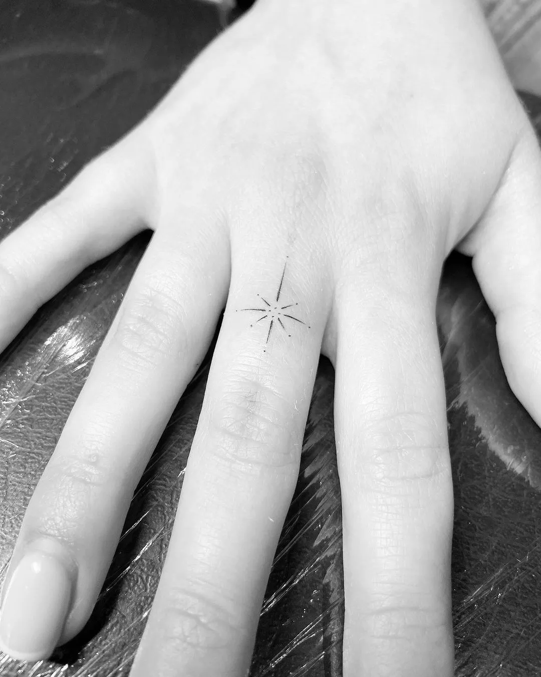 Person showing off the tiny tattoo on their middle finger, which is a slight starburst