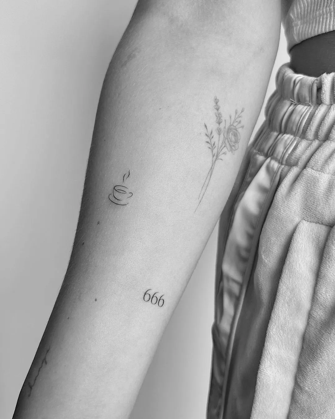 Person shows off their tiny tattoo of a mug on top of a plate with two steam lines coming out of it