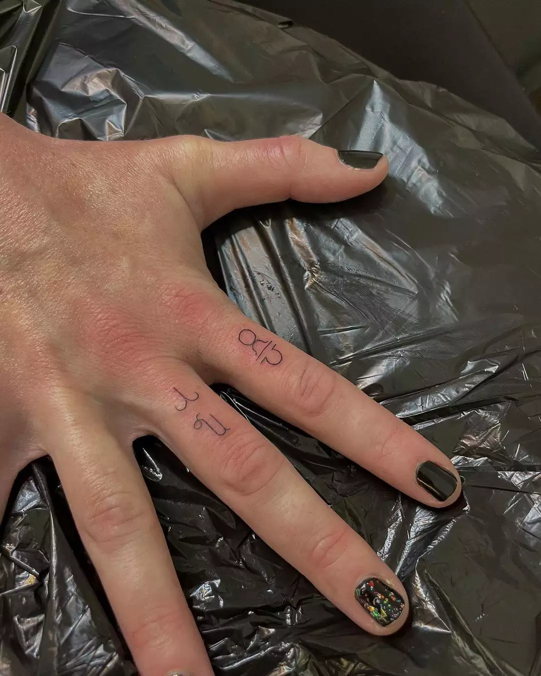Person shows off the tiny tattoos on their middle and index fingers, which are single line symbols