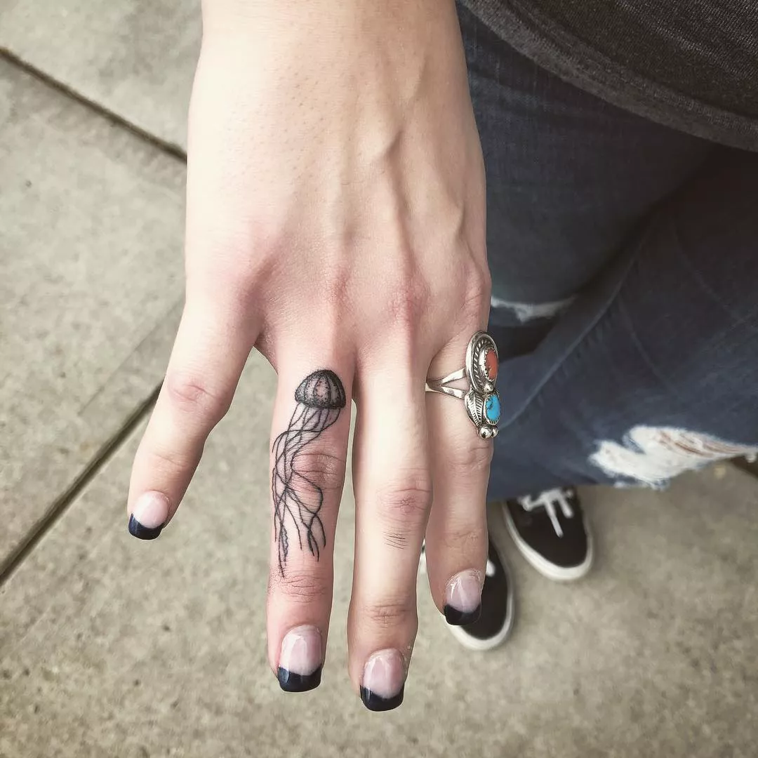 Person shows off the tiny tattoo on their ring finger, which is of a very little jellyfish